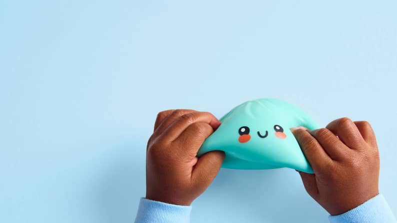 Child hands stretch a teal squishy toy with a smiling face and rosy cheeks.