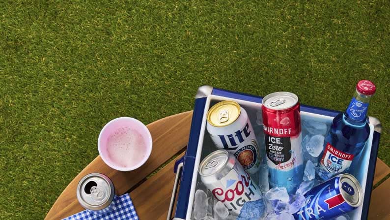 A small cooler of Miller Lite, Coors Light, Smirnoff Ice zero sugar, Smirnoff Ice, and Michelob Ultra next to a plastic cup of beer and a can.