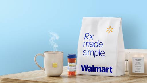 A steaming mug, medication bottle, pharmacy bag and a candle sit on a table.