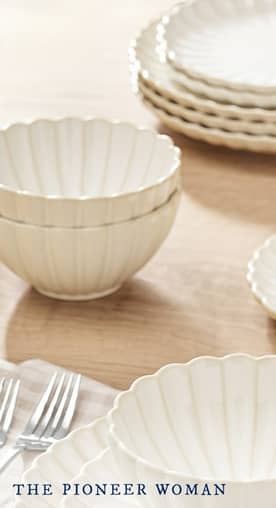 A place setting featuring cream colored dinner plates and bowls with a scalloped design next to two silver forks and a striped napkin.