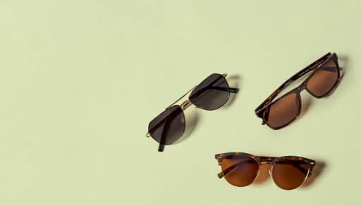 Multiple pairs of sunglasses displayed on a sandy beach.