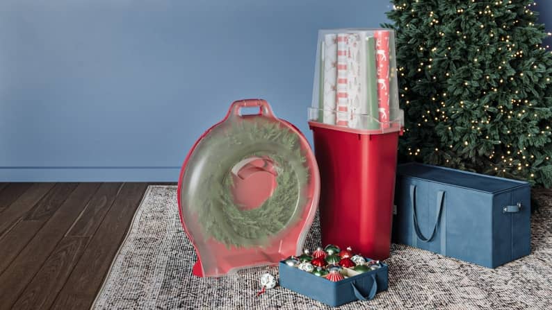 Storage boxes with Christmas decor is shown with a lit Christmas tree in sage blue room.