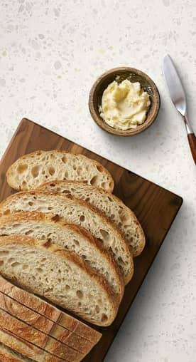 Sliced sourdough is shown on a cutting board with butter & a butter knife.