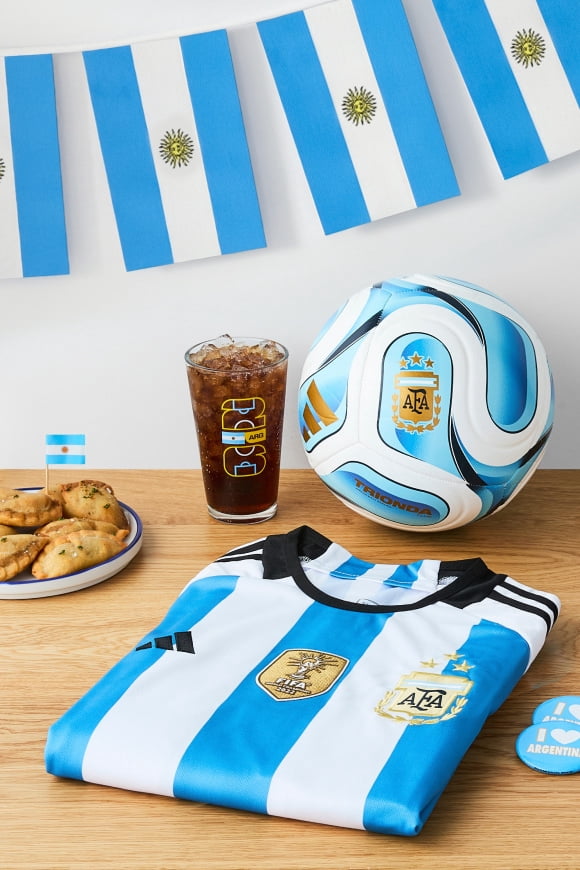 A variety of Team Argentina memorabilia—a plate of empanadas, a cup of cola, I Love Argentina buttons, a jersey, a soccer ball and a flag banner.