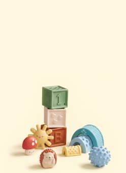 Assorted baby toys including stacking blocks, textured balls and animal figures on a surface.