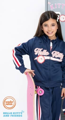 Girl smiles holding a skateboard, wearing a navy Hello Kitty jacket and pants in front of gray school lockers.