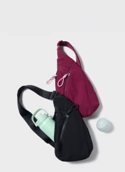 Black sling gym bag holding a mint green water bottle beside a magenta sling bag and tennis ball on a grey backdrop.