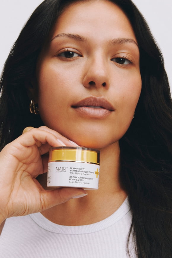 Naia face cream jar with yellow lid held by an adult in a white top.