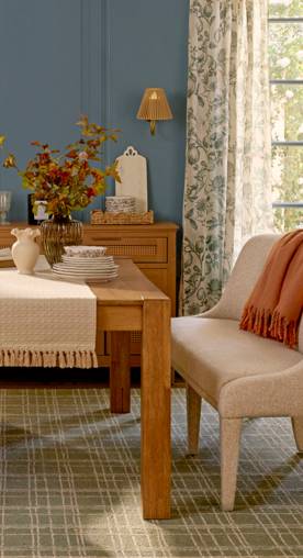 A dining room is set with a wooden table and console with decor and dinnerware. A throw lays on a cream upholstered bench.