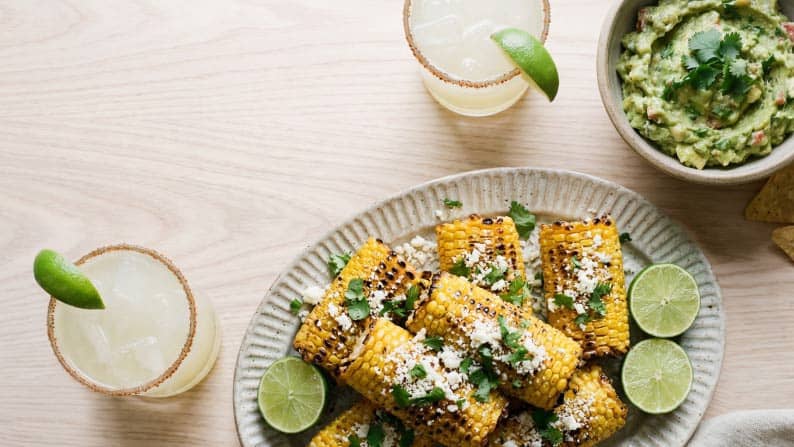 A platter of elote with cotija cheese sprinkle, next to a bowl of guacamole.