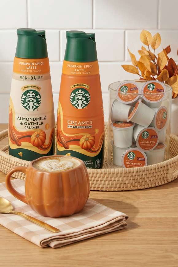 A pumpkin-shaped mug of coffee next to regular and non-dairy Starbucks pumpkin spice creamers and a jar of Starbucks pumpkin spice K Cups.