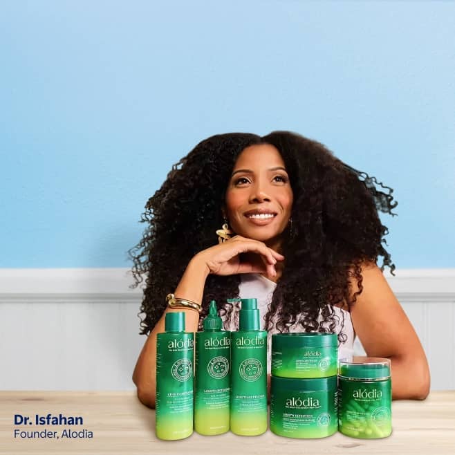 Doctor Isfahan, the founder of Alodia haircare, is pictured posing above an assortment of Alodia hair products organized on a table.