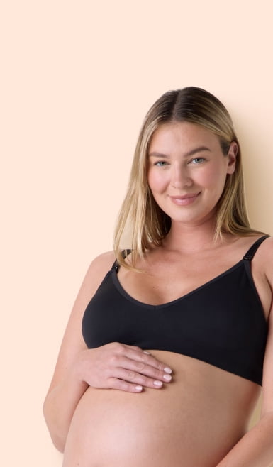 Pregnant adult wearing a black maternity bra, smiling and resting hands on bare belly.