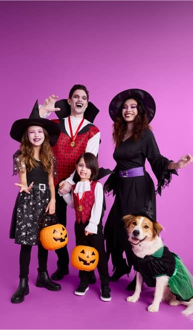 Family shown wearing witch and vampire costumes with a dog in a witch costume.