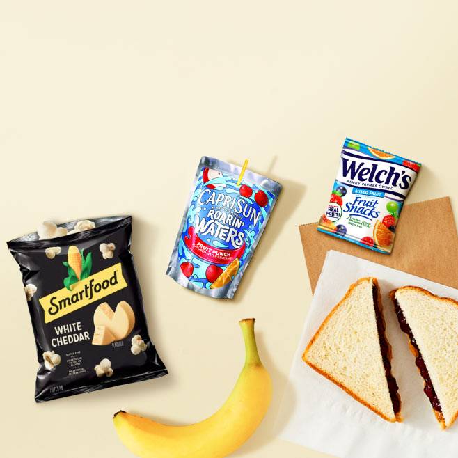 Smartfood white cheddar popcorn, Capri-Sun fruit punch, Welch’s fruit snacks, a peanut butter and jelly sandwich, and a banana are shown.