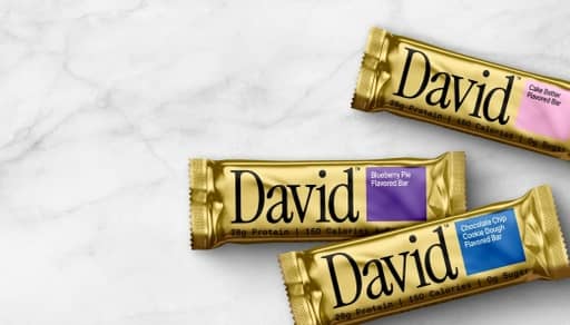 Three David protein bars with gold wrapping on a marble surface