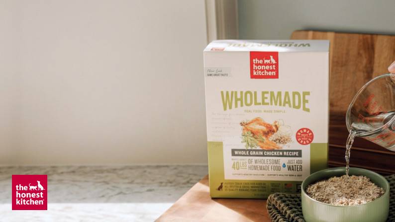 The Honest Kitchen brand logo. Whole grain chicken recipe pet food packaging and a filled bowl is shown.