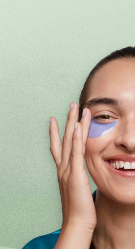 Image shows a smiling woman wearing eye gel patches.