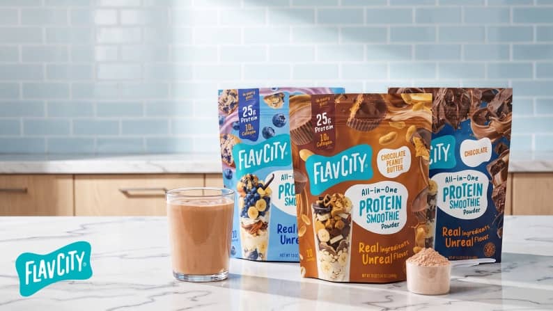 Flavcity All in One Protein Smoothie powder pouches with chocolate, peanut butter and berry visuals beside a glass shake and scoop of powder.