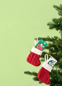 An image of Snoopy and Starbucks gift cards in Christmas stocking ornaments, hanging on a tree with white lights.