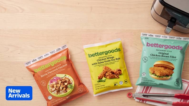 New Arrivals badge. Three Bettergoods frozen chicken bags on a wooden surface with an air fryer and red kitchen utensils.