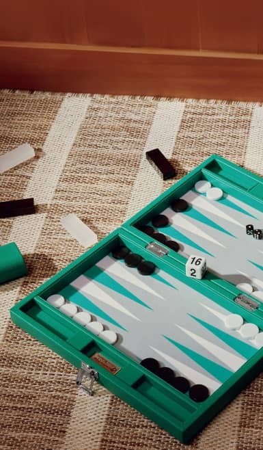 Open backgammon board game with green case, dice, and playing pieces on a woven rug.