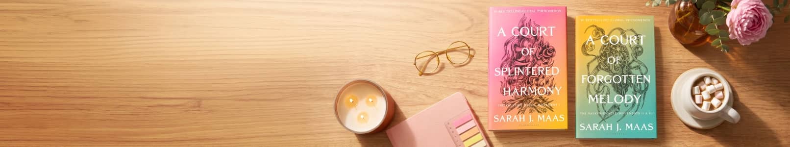 Sarah J. Maas books A Court of Shattered Vows and A Court of Forgotten Melody on a wooden desk with glasses, candle and flowers.