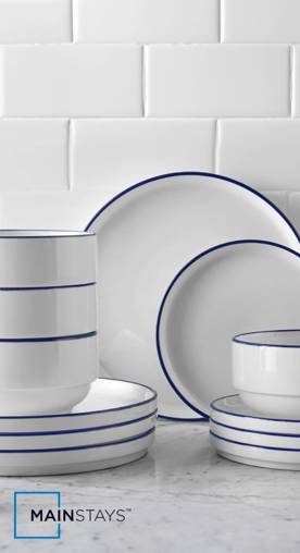 A set of white ceramic dinnerware with blue trim is shown on a white marble countertop against white subway tile.