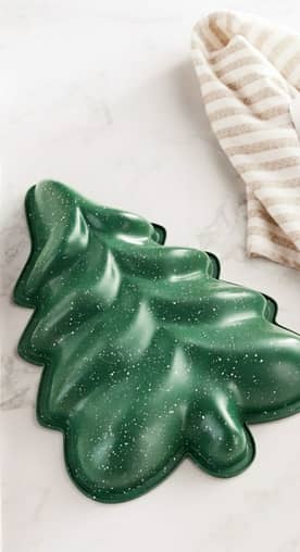 A green baking mold in the shape of a Christmas tree. A striped tea towel is beside it.