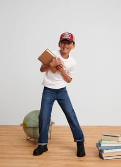 A boy in straight-leg jeans, white tee, black boots and a cap.