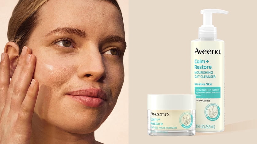 Model applying moisturizer on her face next to Aveeno Calm and Restore gel moisturizer and oat cleanser.