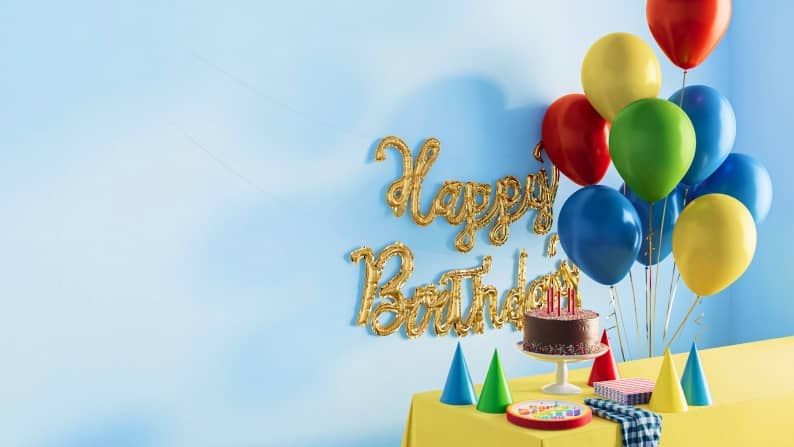 A birthday party setup featuring a chocolate cake, balloons, and a happy birthday sign.