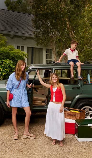 A family of four is wearing red, white and blue outfits posing in front of a green SUV outside of a house.