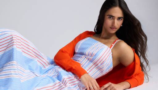 A woman in an unbuttoned orange cardigan over a red, blue and white striped dress, laying down and posing.