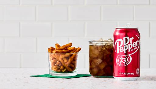 A clear cup of pretzel twists next to a glass and can of Dr. Pepper are shown on a white quartz countertop against a white tile backsplash.