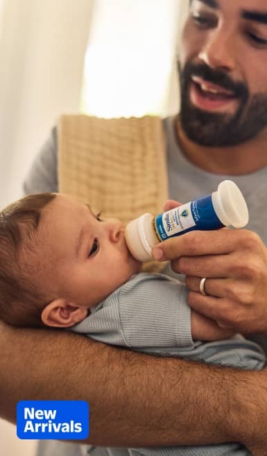 New Arrivals badge. Adult feeds baby with a bottle while holding the child.