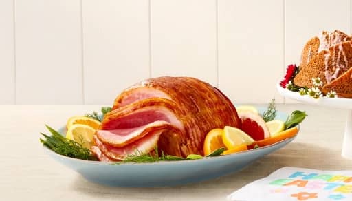 A baked spiral ham is pictured on a serving tray with fresh garnish.