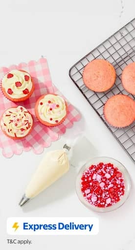 Express Delivery. T and C apply. Decorated and plain strawberry cupcakes on a counter next to a bag of icing and a bowl of sprinkles.