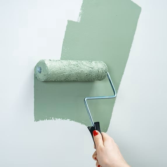 A paint roller painting green paint on a white wall