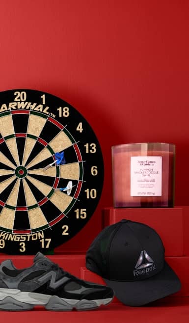 An image of a dart board with two darts, Better Homes & Gardens candle, Reebok hat and New Balance sneakers.