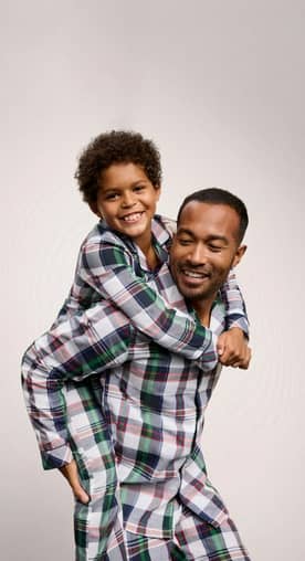 A father and son wearing matching plaid pajamas are pictured on a beige backdrop.