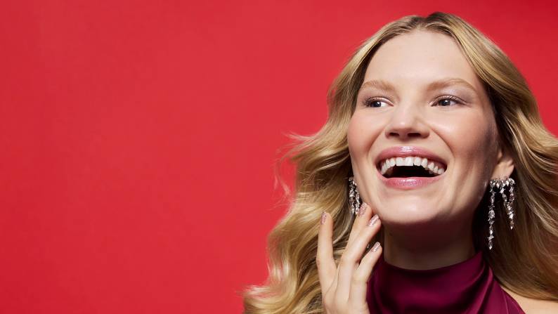 A close-up of a woman smiling and looking away with her hand on her face.