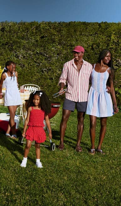 A family of four is wearing red, white and blue outfits on the lawn together.