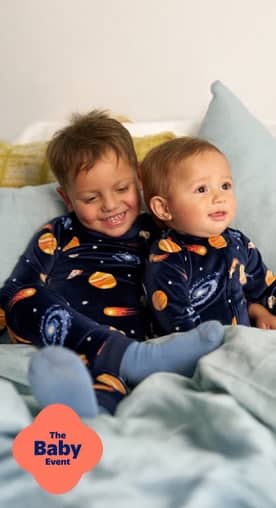 The Baby Event logo. Two little boys wearing blue planet-printed pajamas are hugging, while sitting on a bed.