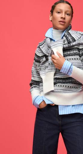 Woman wearing a grey striped sweater with another one over her shoulders, layered over a blue striped shirt and white turtleneck.
