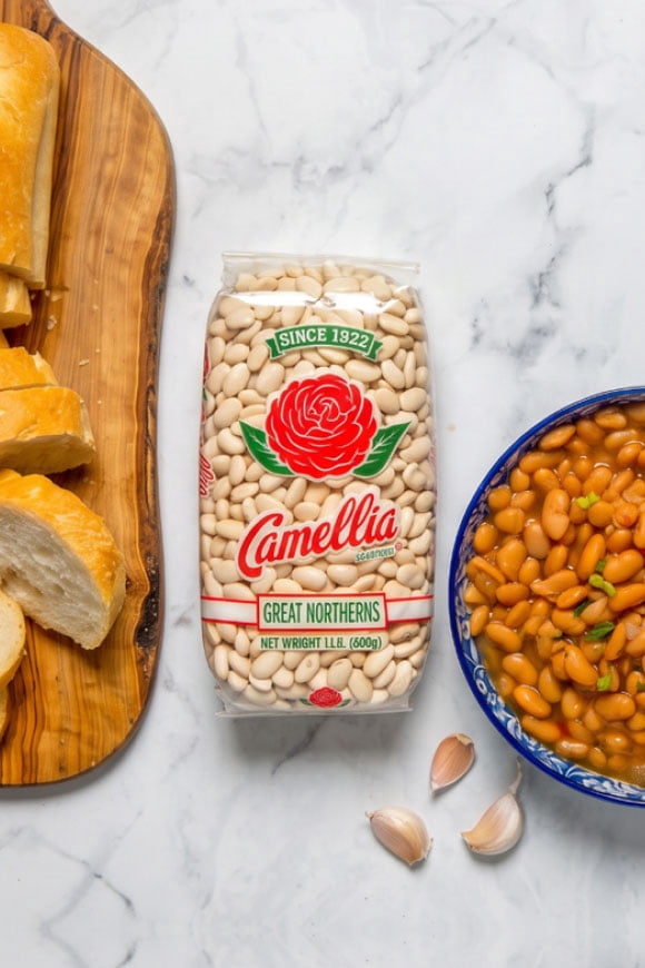 Camellia Great Northerns dry beans bag between sliced bread and a blue bowl of cooked beans with green onions and garlic cloves.
