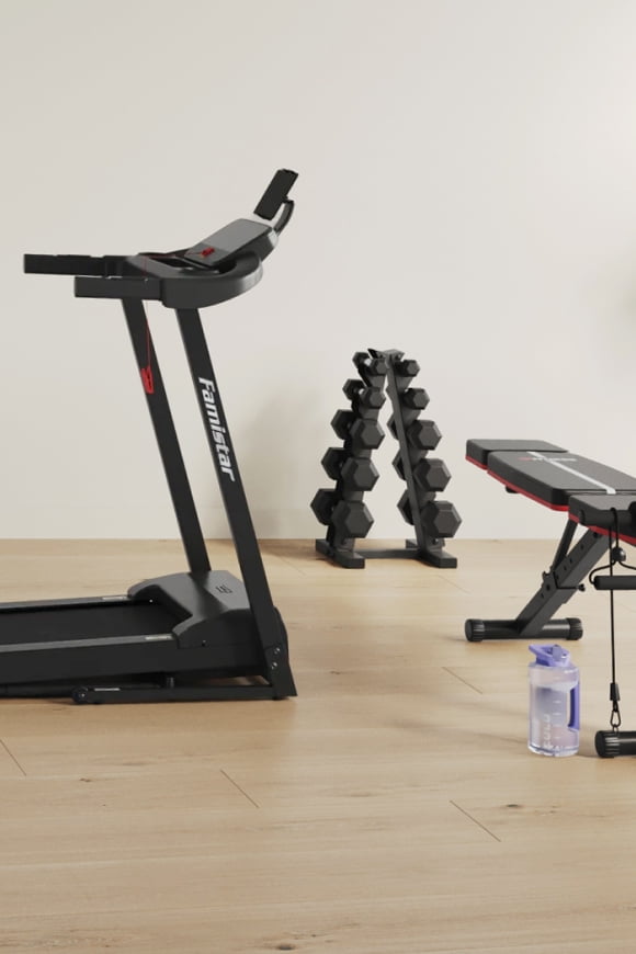 An image of a treadmill, a weight bench and weights on a light wood floor in a beige room.