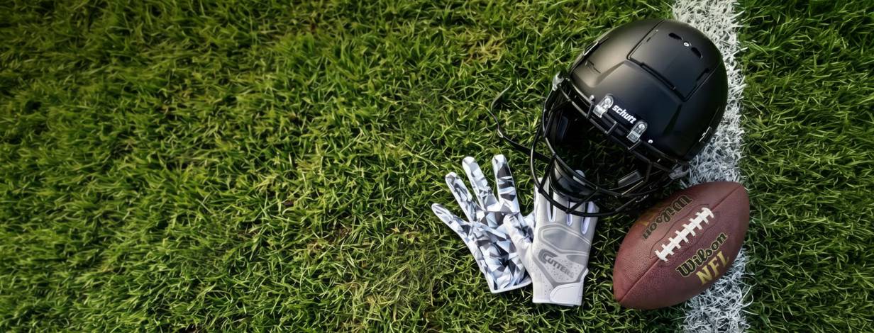 A football helmet, gloves and a ball on grass.