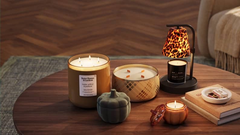 A coffee table displays lit candles, a pumpkin, books and a patterned lamp in a cozy living room.
