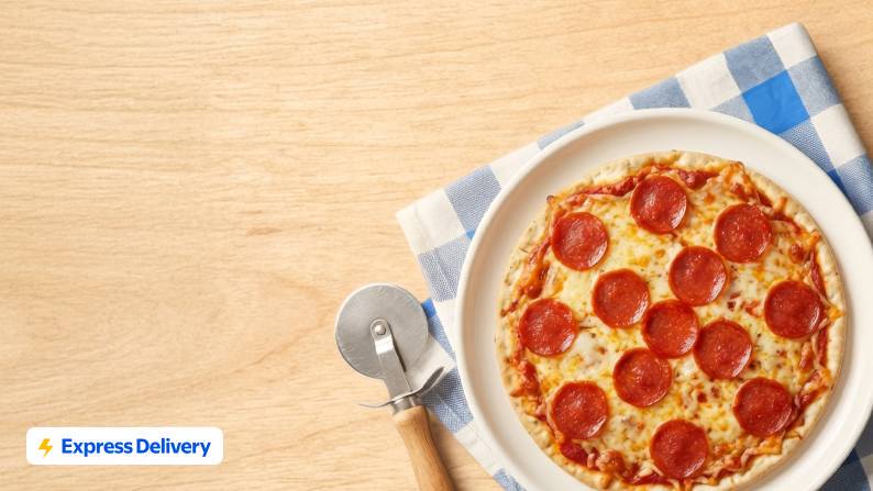 Express Delivery. A white plate with a whole pepperoni pizza on it on top of a blue and white checked kitchen towel next to a pizza cutter.